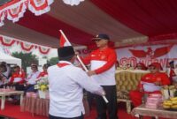 Bupati Bone Bolango, Drs. H. Ismet Mile, MM, saat menerima bendera Merah Putih dalam Apel Gerakan Pembagian Benderah Merah Putih Tahun 2025 tingkat Kabupaten Bone Bolango yang digelar di Danau Perintis Desa Boludawa, Jum'at 1 Agustus 2025. 